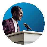 The image shows a man in front of a podium giving a speech. The image is in a blue circle.
