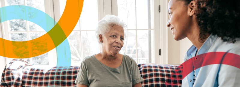 An older Black woman talks to her direct care worker in her home